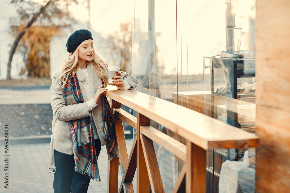 Elegant lady in a winter city. Stylish girl drinking a coffee.  Blonde in a cute beret