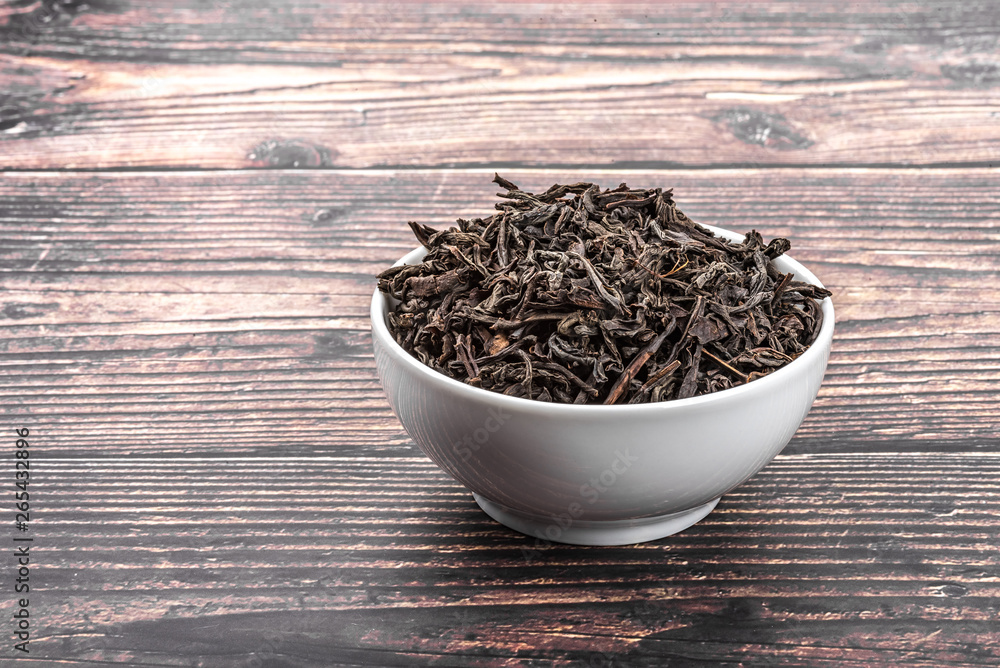Fototapeta premium Dried tea is poured into a ceramic cup on a wooden plank table.