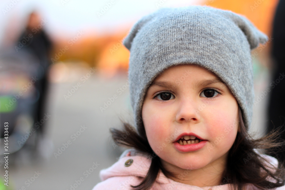 Evening portrait of a beautiful little girl in a hat and coat on the background of the urban landscape in sunset light. Evening portrait of a beautiful little girl in a hat and coat on the background of the urban landscape in sunset light.