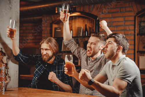 Sports fans funny friends men sit in bar drink beer and watch football match on TV in pub
