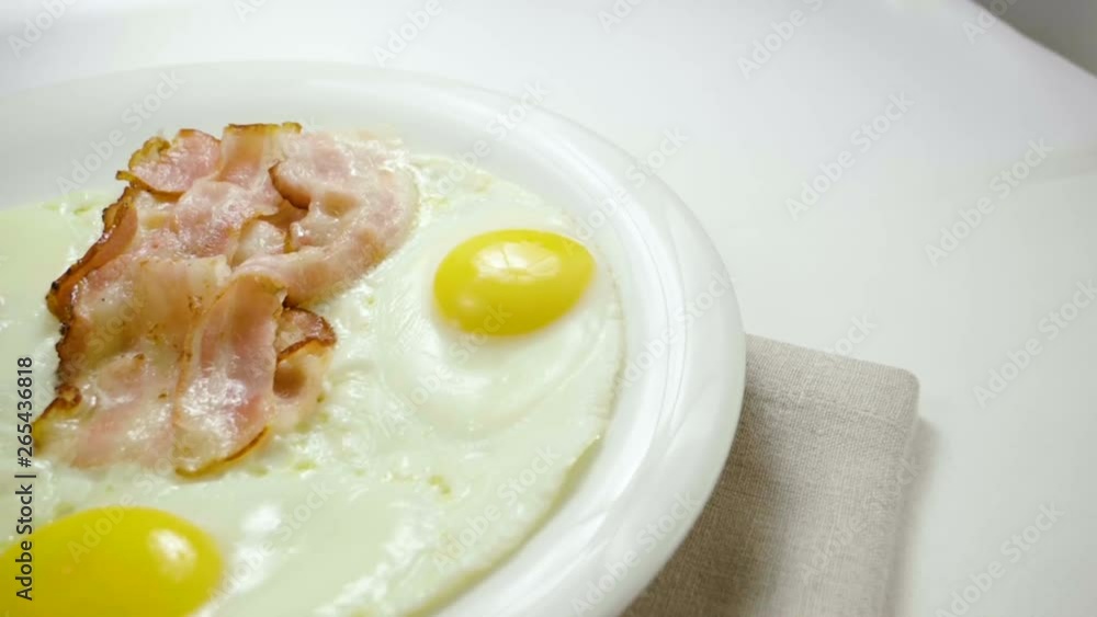 Close-up shot of three fried eggs and bacon serving on a white plate for breakfast. Slow motion. HD Close-up shot of three fried eggs and bacon serving on a white plate for breakfast. Slow motion. HD