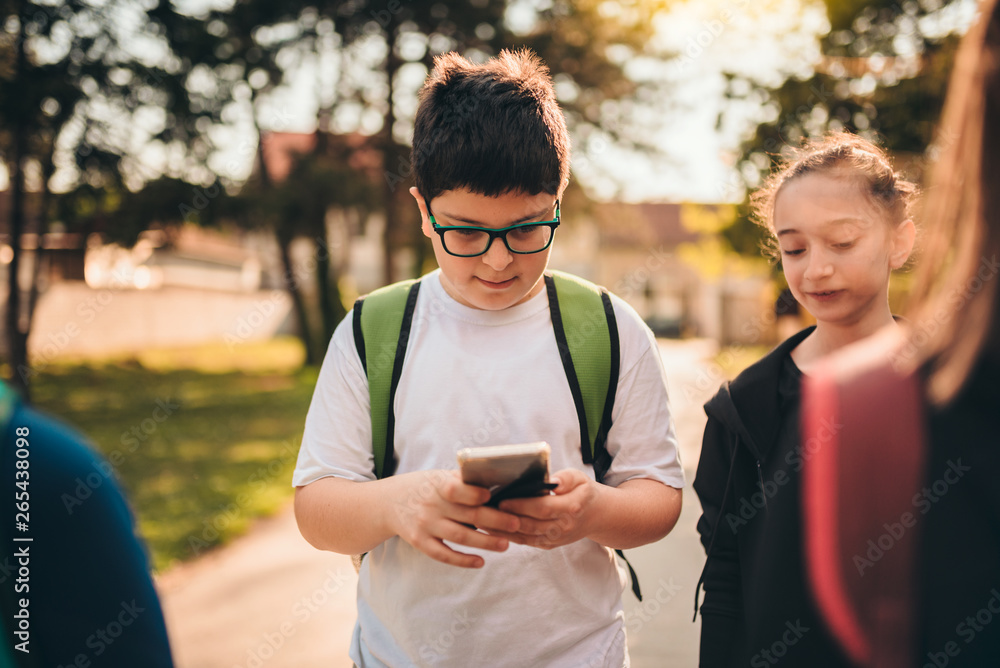 Boy standing with classmates using smart phone at schoolyard Boy standing with classmates using smart phone at schoolyard