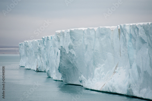 View along glacier wall from sea with still sea under bottom ledge in northern arctic, atmospheric image of climate change issue.