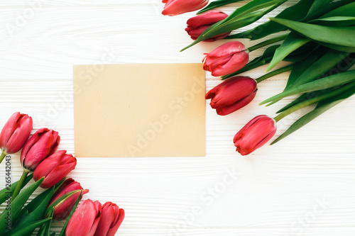Fototapeta Naklejka Na Ścianę i Meble -  Beautiful red tulips and craft card with space for text on white wooden background, flat lay. Happy Mothers day. Pink tulips on white wood. Greeting card template. Valentines day