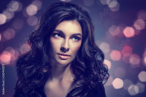 A beautiful woman with a doll face and gorgeous dark hair against the background of bright lights.