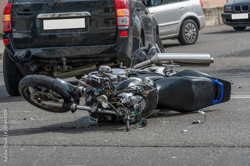 broken motorcycle closeup beside the car. an accident on the road in the city on a sunny day involving a motorcycle and a car. photo