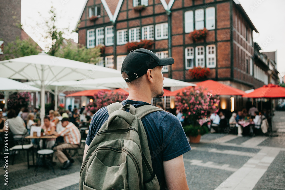 Tourist or student with a backpack in the city of Muenster in Germany and looking for where to dine. Ahead is a street cafe with unrecognizable people