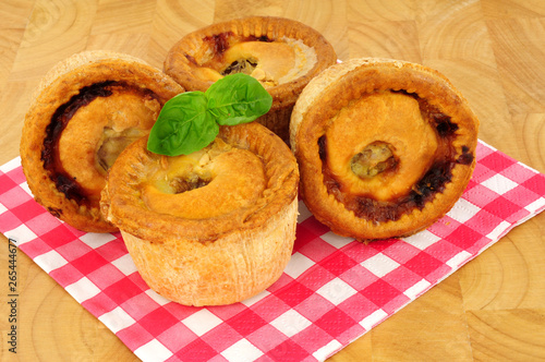 Group of savoury crusty pork pies on a paper gingham pattern napkin with a wood background