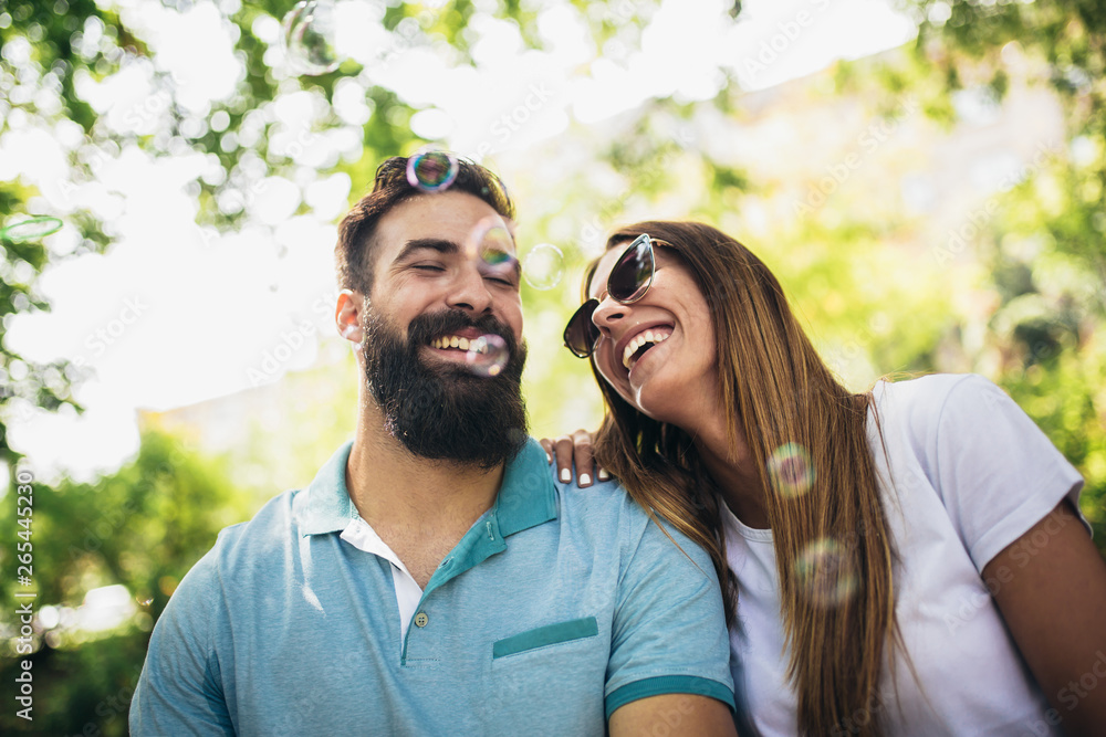 Couple sitting on the park bench and blowing soup bubbles on beautiful sunny day Couple sitting on the park bench and blowing soup bubbles on beautiful sunny day