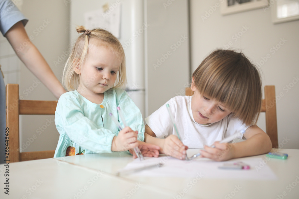 Children siblings paint at table in white kitchen Children siblings paint at table in white kitchen