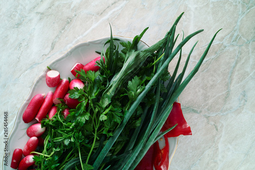 Plate with fresh greens, radish and bell pepper slices. Parsley, green onions, tarragon, radish and bell pepper on a plate