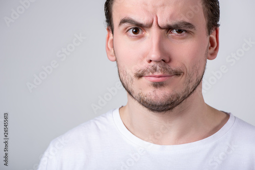 Handsome guy with bristles in a white T-shirt makes funny grimaces on his face