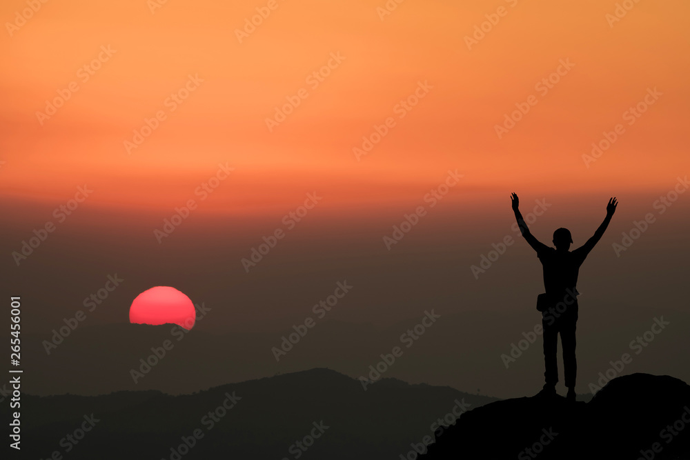 Silhouette of man hold up hands on the peak of mountain.