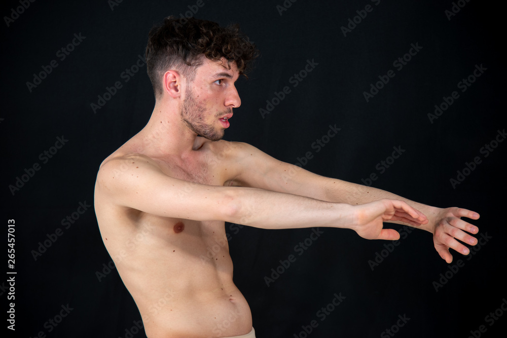 Half-naked portrait of a young male dancer, in movements relating to dancing with his hands. The attractive young man with beard in modern dance demonstrations on a black background.