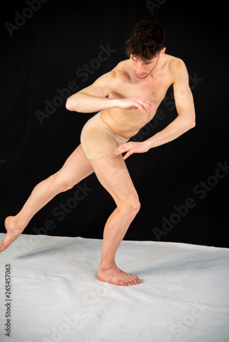 The gymnastic pose of the Caucasian man dances in the studio with plastic hand and leg positions. The attractive young man shows modern dance poses, on a black background.