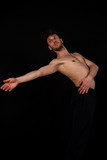 Male dancer with black trousers and bare chest, practicing in the studio on a black background. The attractive young man shows modern dance poses.