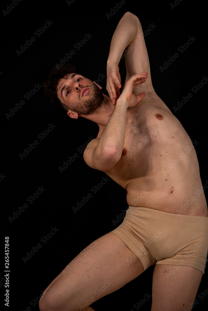 Half-naked portrait of a young male dancer, in movements relating to dancing with his hands. The attractive young man with beard in modern dance demonstrations on a black background.