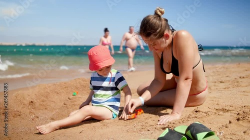 4k video of little toddler boy playing with his mother on ea beach. FAmily playing toys and relaxing on summer vacation photo