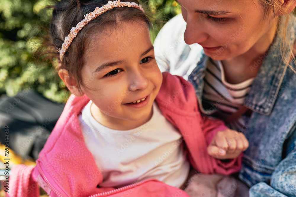 Closeup portrait of young woman with her little cute daughter are spending time together outdoors. Mom with her toddler kid girl in park, smiling, feeling happy and loving each other. Childhood Closeup portrait of young woman with her little cute daughter are spending time together outdoors. Mom with her toddler kid girl in park, smiling, feeling happy and loving each other. Childhood