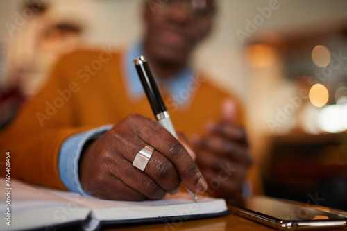 Close up of contemporary African man holding pen while working sitting at table in cafe, copy space