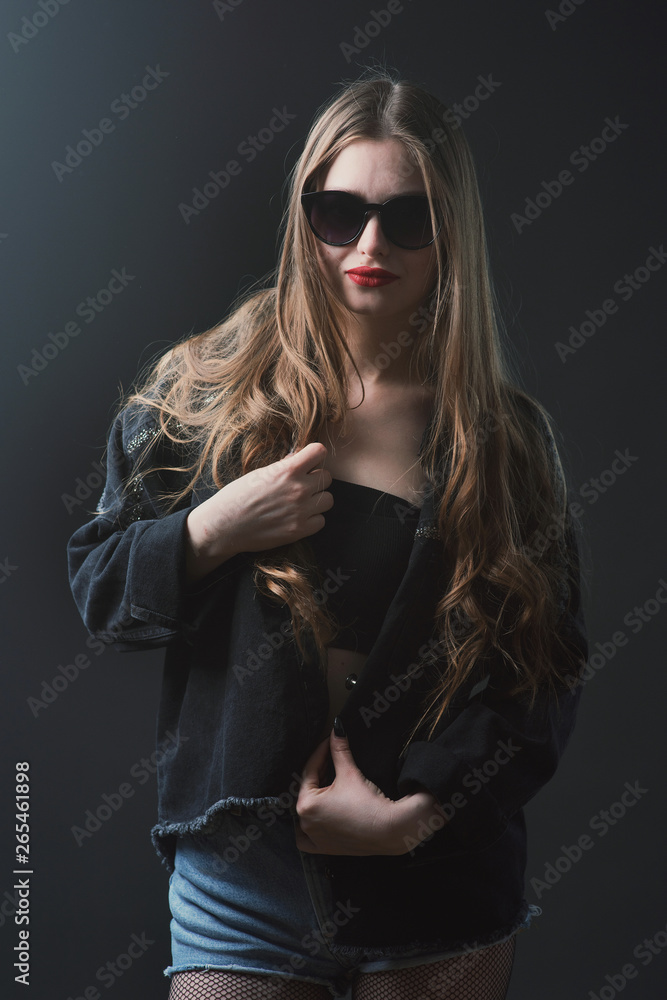 Young beautiful, slender, passionate brown-haired woman with bright red lips and long hair in a black top and denim shorts on a dark background Young beautiful, slender, passionate brown-haired woman with bright red lips and long hair in a black top and denim shorts on a dark background