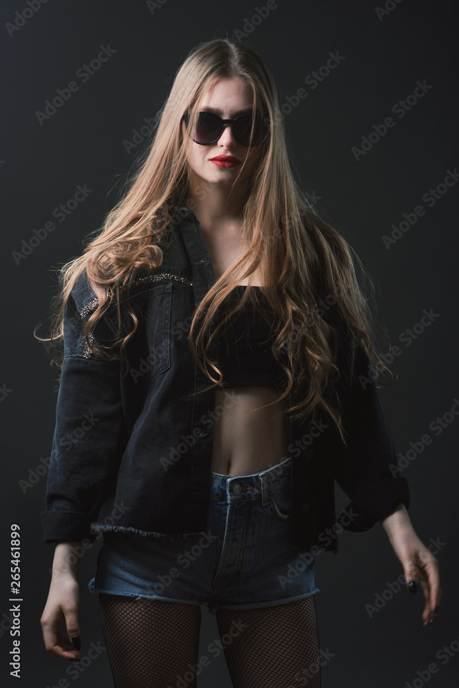 Young beautiful, slender, passionate brown-haired woman with bright red lips and long hair in a black top and denim shorts on a dark background Young beautiful, slender, passionate brown-haired woman with bright red lips and long hair in a black top and denim shorts on a dark background