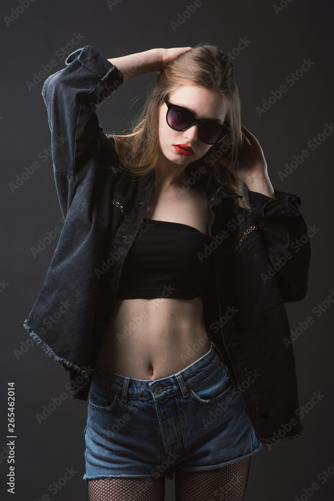 Young beautiful, slender, passionate brown-haired woman with bright red lips and long hair in a black top and denim shorts on a dark background Young beautiful, slender, passionate brown-haired woman with bright red lips and long hair in a black top and denim shorts on a dark background