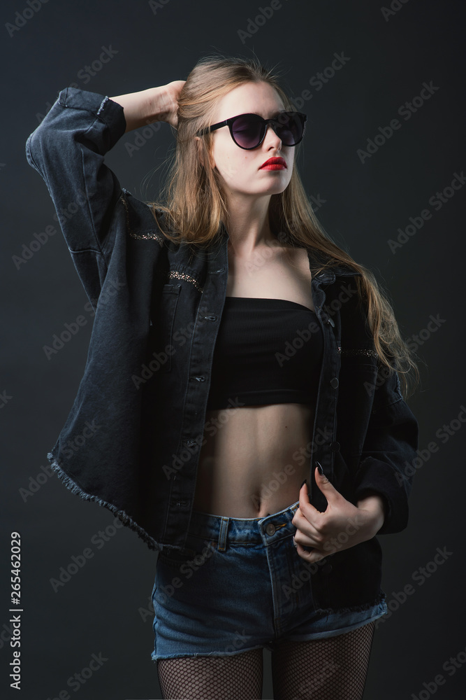 Young beautiful, slender, passionate brown-haired woman with bright red lips and long hair in a black top and denim shorts on a dark background Young beautiful, slender, passionate brown-haired woman with bright red lips and long hair in a black top and denim shorts on a dark background