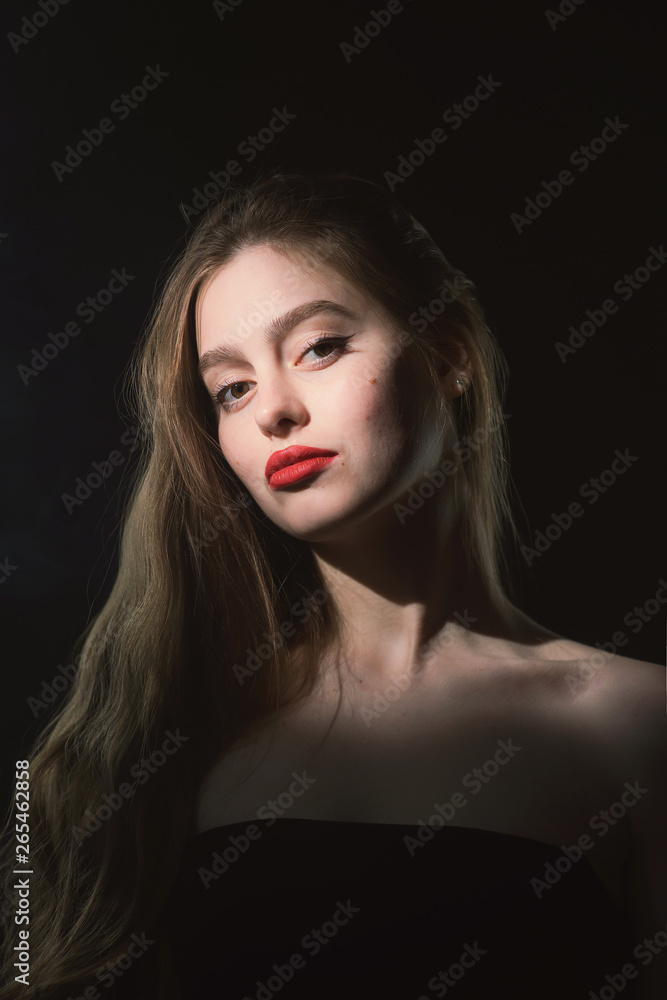 Young beautiful, slender, passionate brown-haired woman with bright red lips and long hair in a black top and denim shorts on a dark background Young beautiful, slender, passionate brown-haired woman with bright red lips and long hair in a black top and denim shorts on a dark background
