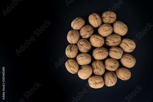 Walnuts in shell lying in the center on black surface, top view. Background of round walnuts. Healthy nuts and seeds composition.