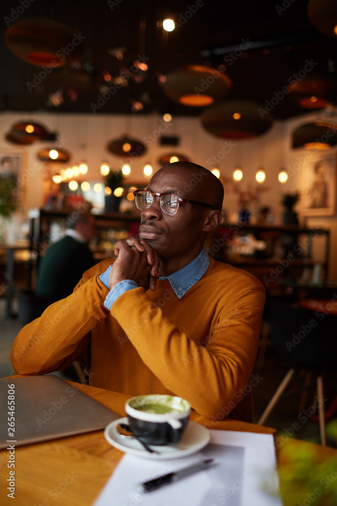 Warm toned portrait of pensive African-American man using laptop sitting at table in cafe