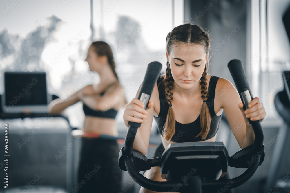 Attractive woman biking in the gym, exercising legs doing cardio workout cycling bikes. Fitness club with training exercise bikes. Fitness, Healthy, Sport, Lifestyle concept. Attractive woman biking in the gym, exercising legs doing cardio workout cycling bikes. Fitness club with training exercise bikes. Fitness, Healthy, Sport, Lifestyle concept.