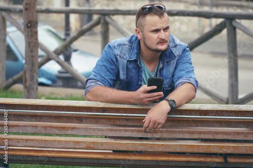 Young man is sitting at the park and using smartphone, phone, calls. concept of remote work, and finding information on the journey