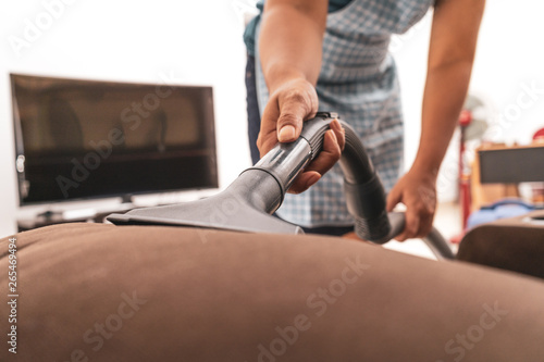 Close up of young woman cleaning sofa with vacuum cleaner at home © Gayan