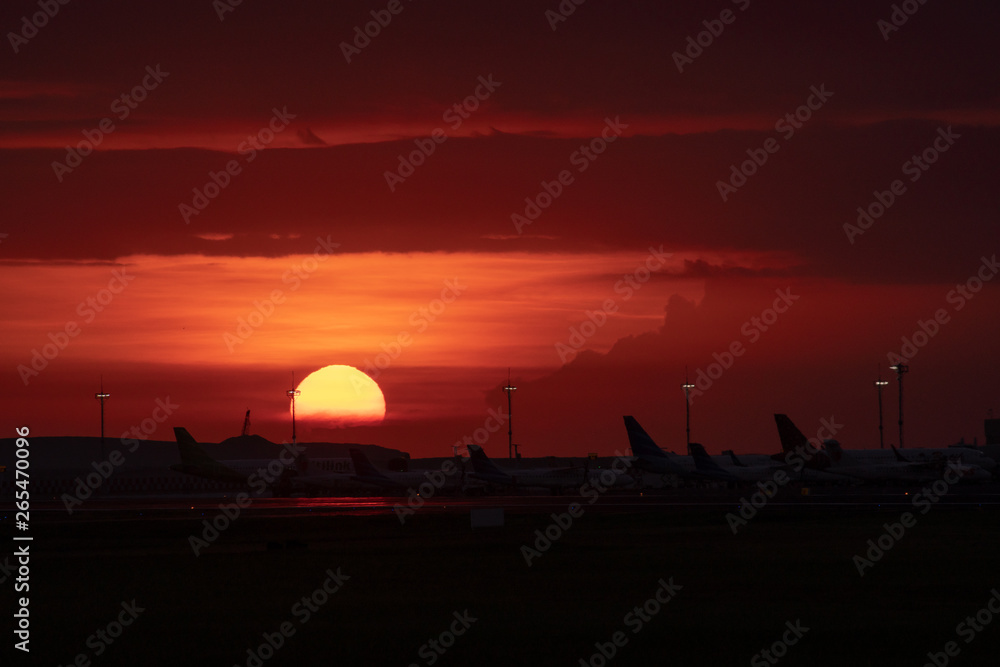the twilight sky in an airport is decorated with sunsets which start to sink golden orange with silhouettes of aircraft activities around the airport