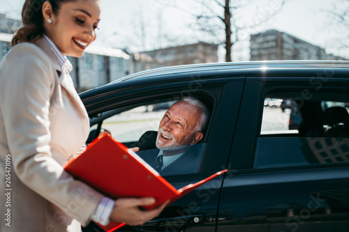 Obraz na plátně Beautiful young woman sales manager showing car specification to happy senior man buyer