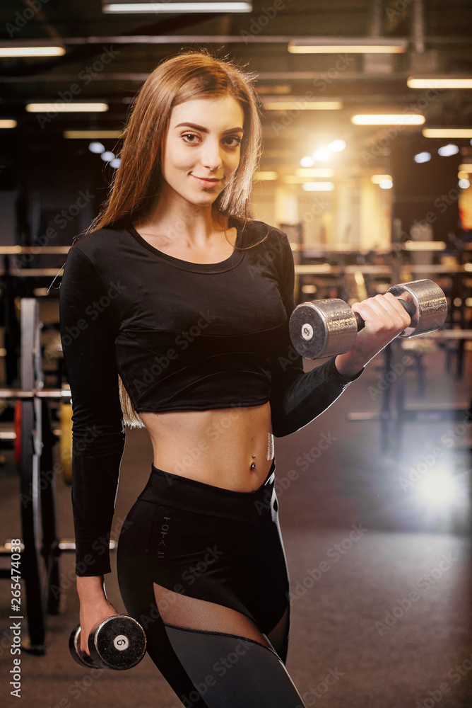 Young girl playing dumbbell to exercise in fitness. Photo of sporty caucasian woman in sportswear. Strong abs showing. Noise photo Young girl playing dumbbell to exercise in fitness. Photo of sporty caucasian woman in sportswear. Strong abs showing. Noise photo