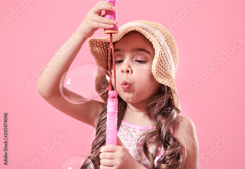 little girl blowing soap bubbles on colored background photo