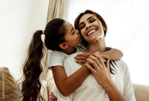 Family. Love. Togetherness. Mom and daughter at home. Girl is kissing her mom in cheek, woman is smiling