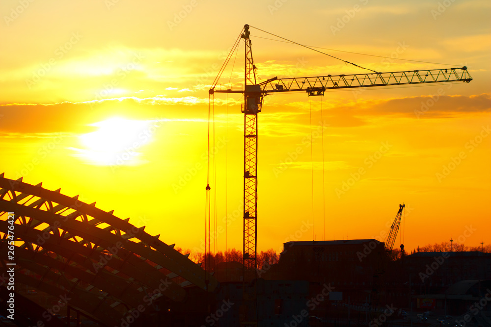 Industrial machinery, construction crane. Cranes and frame sports arena under construction, city skyline at sunset, sunrise Building under Construction site. 