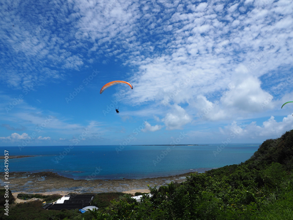 A man flying in the beautiful blue cloudy beautiful sky withe the sea and the mountain background, parachute with a motor, paramotor. Sky driving. Extreme sport, adventure, freedom concept. A man flying in the beautiful blue cloudy beautiful sky withe the sea and the mountain background, parachute with a motor, paramotor. Sky driving. Extreme sport, adventure, freedom concept.