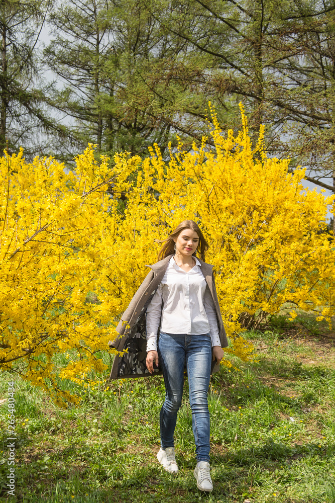 A girl walks past bright yellow bushes. Spring happy lifestyle A girl walks past bright yellow bushes. Spring happy lifestyle