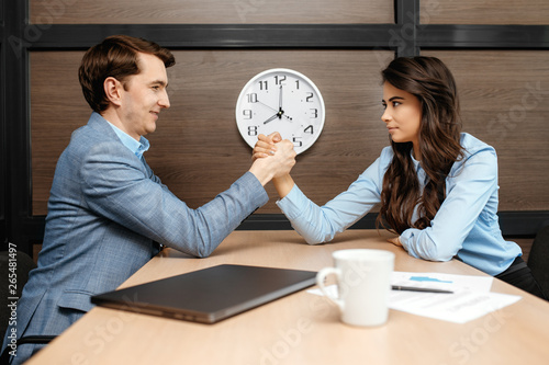 Photo of two business colleagues arm wrestling on desk in modern office.