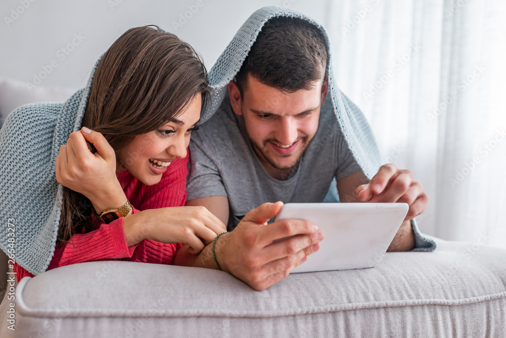 Leisure and technology in the bed. Couple having fun with digital tablet in bed. Close up view of beautiful smiling young wife and husband looking a tablet Leisure and technology in the bed. Couple having fun with digital tablet in bed. Close up view of beautiful smiling young wife and husband looking a tablet