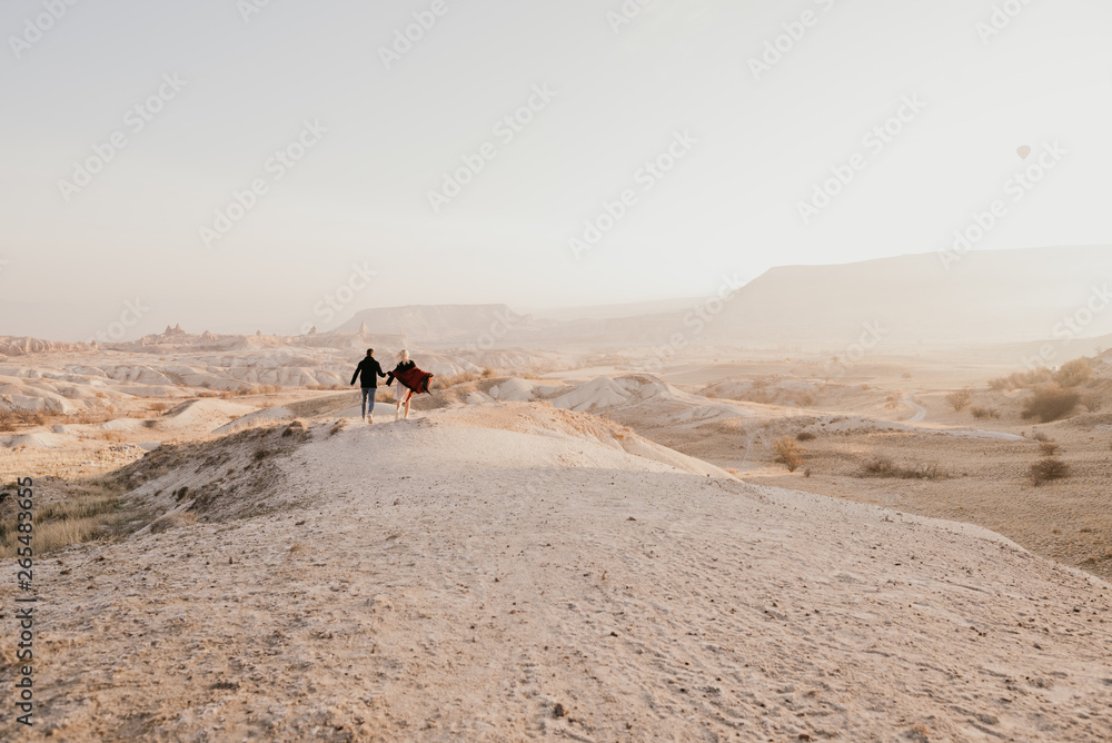 Young couple running into the distance among mountains and sand in Cappadocia, Turkey Young couple running into the distance among mountains and sand in Cappadocia, Turkey