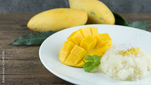The close up of heap yellow mango and sticky rice setting with coconut milk in the dish on wooden table. popular traditional dessert of Thailand.