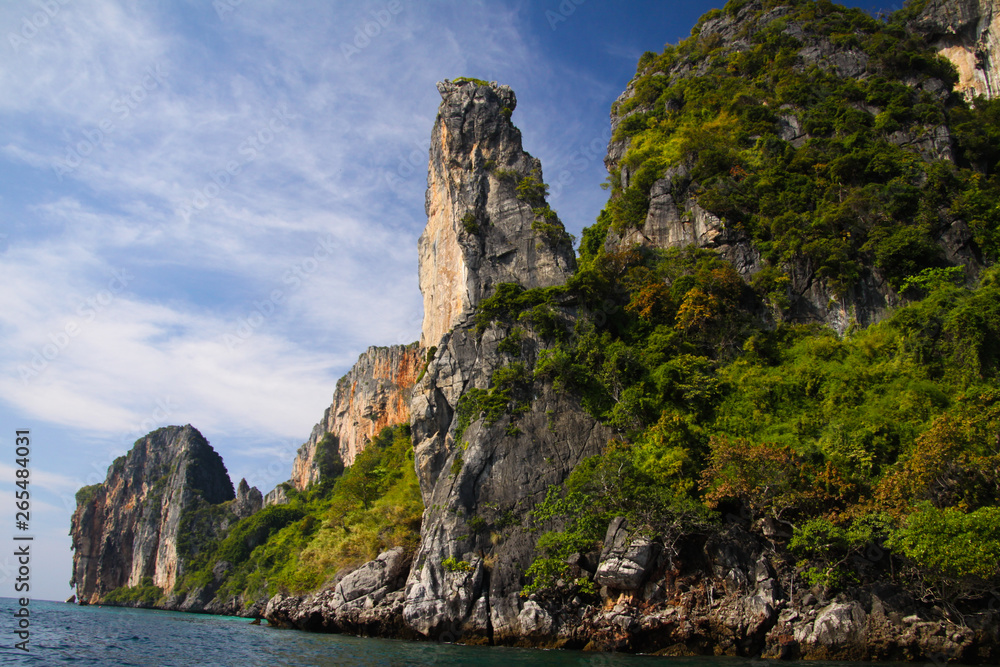 Boat trip along the coast line of tropical island Ko Phi Phi along impressive rock formations under blue sky