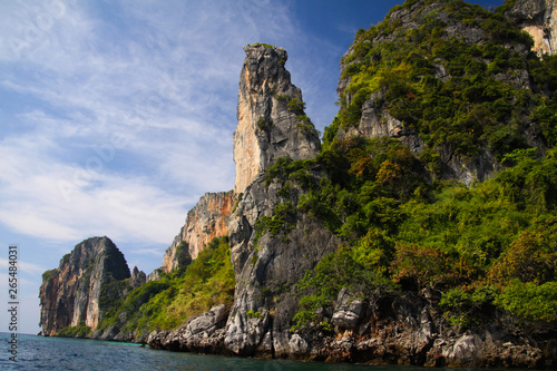 Boat trip along the coast line of tropical island Ko Phi Phi along impressive rock formations under blue sky