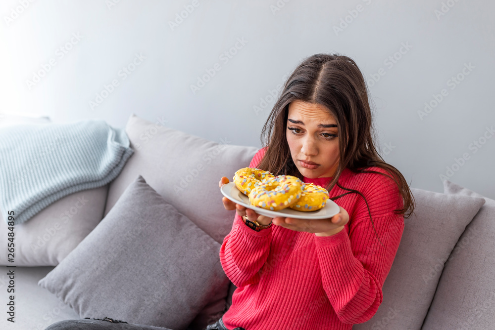 Woman on diet caught during eating unhealthy donut. Beautiful girl is looking at unhealthy donut with appetite. Woman and donut close-up Woman on diet caught during eating unhealthy donut. Beautiful girl is looking at unhealthy donut with appetite. Woman and donut close-up