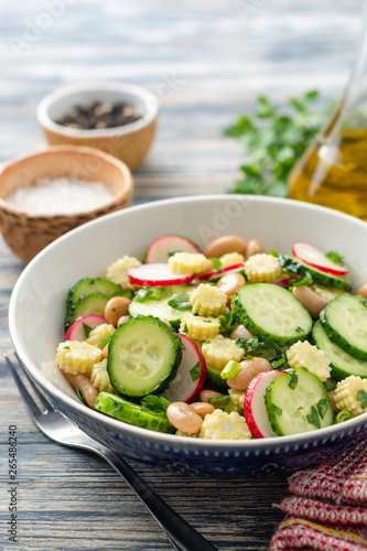 Healthy vegetable salad with cucumber, radish, beans, mini corn and herbs on rustic wooden background. Selective focus.